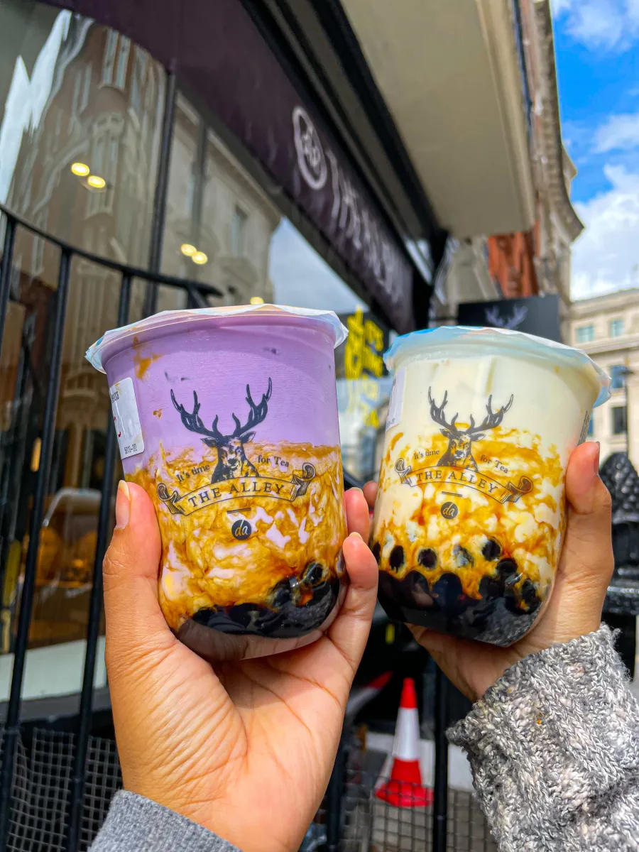 Holding two Alley Drinks, Ube Boba on the left and Brown Sugar Boba on the right